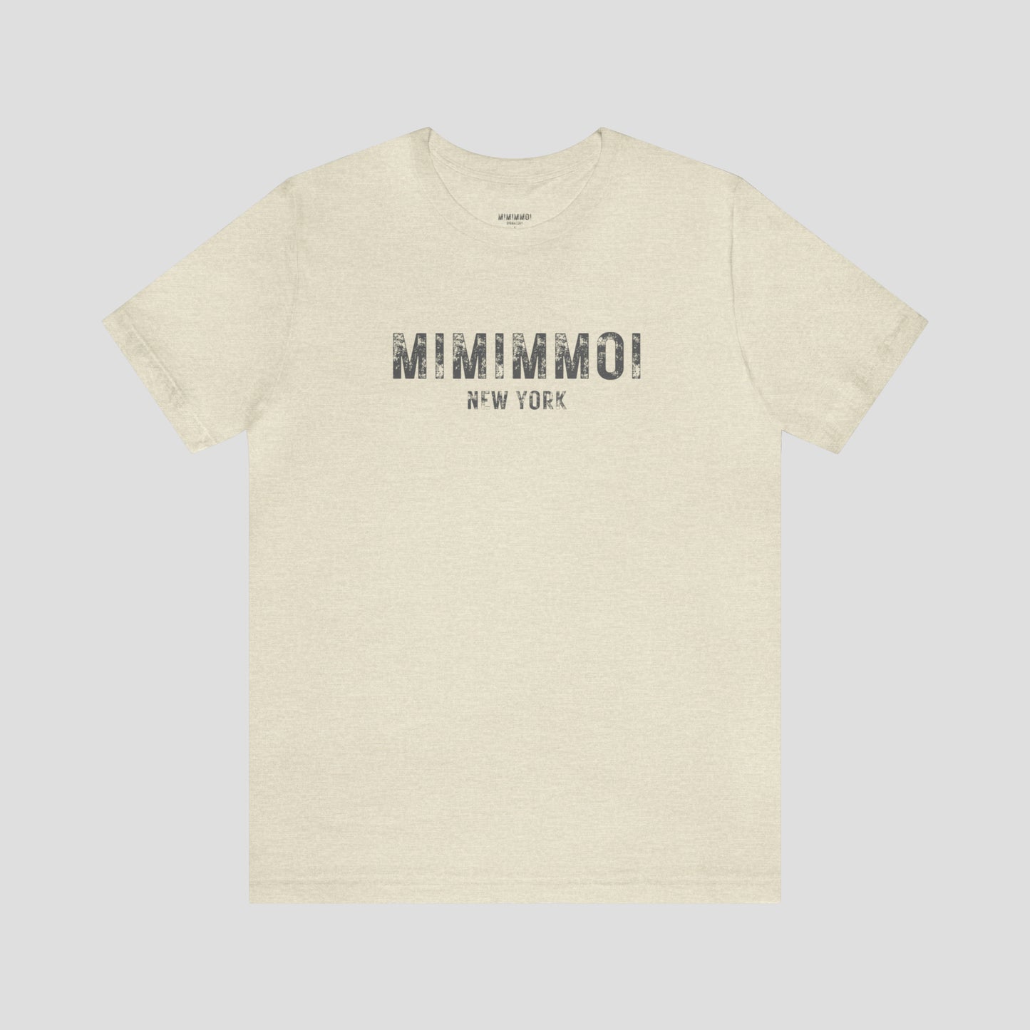 Natural tan-colored t-shirt with the words Mimimmoi New York in distressed gray block letters across the chest, against a gray background.
