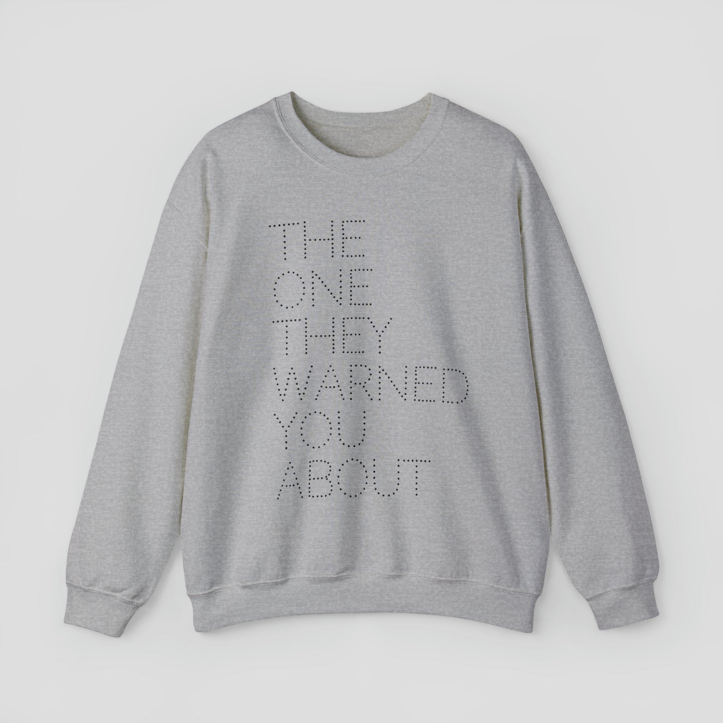 Front view of dark gray sweatshirt with with the words "The One They Warned You About" in capitalized dotted text in center, against a gray background.
