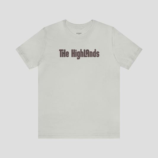 Silver-grey t-shirt with the words "The Highlands" in violet letters across the chest, against a gray background.