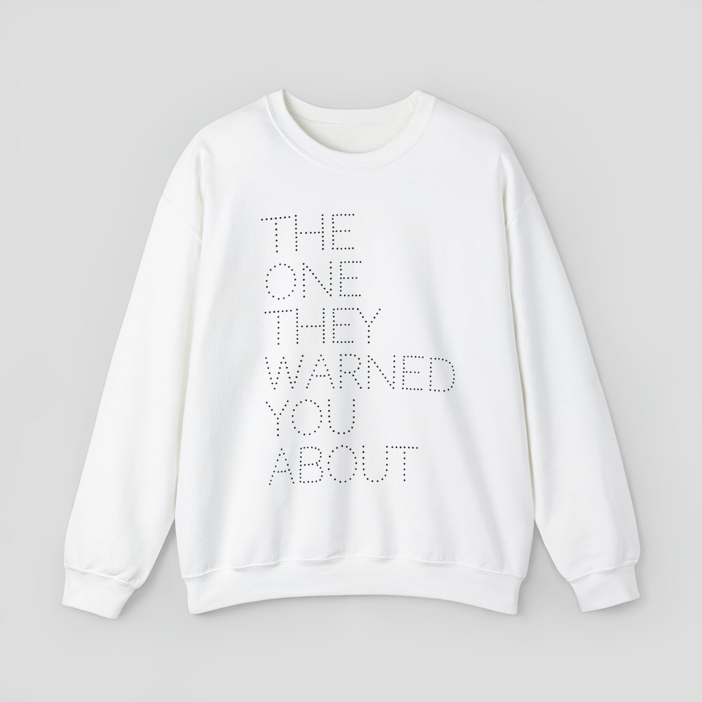 Front view of white sweatshirt with with the words "The One They Warned You About" in capitalized dotted text in center, against a gray background.