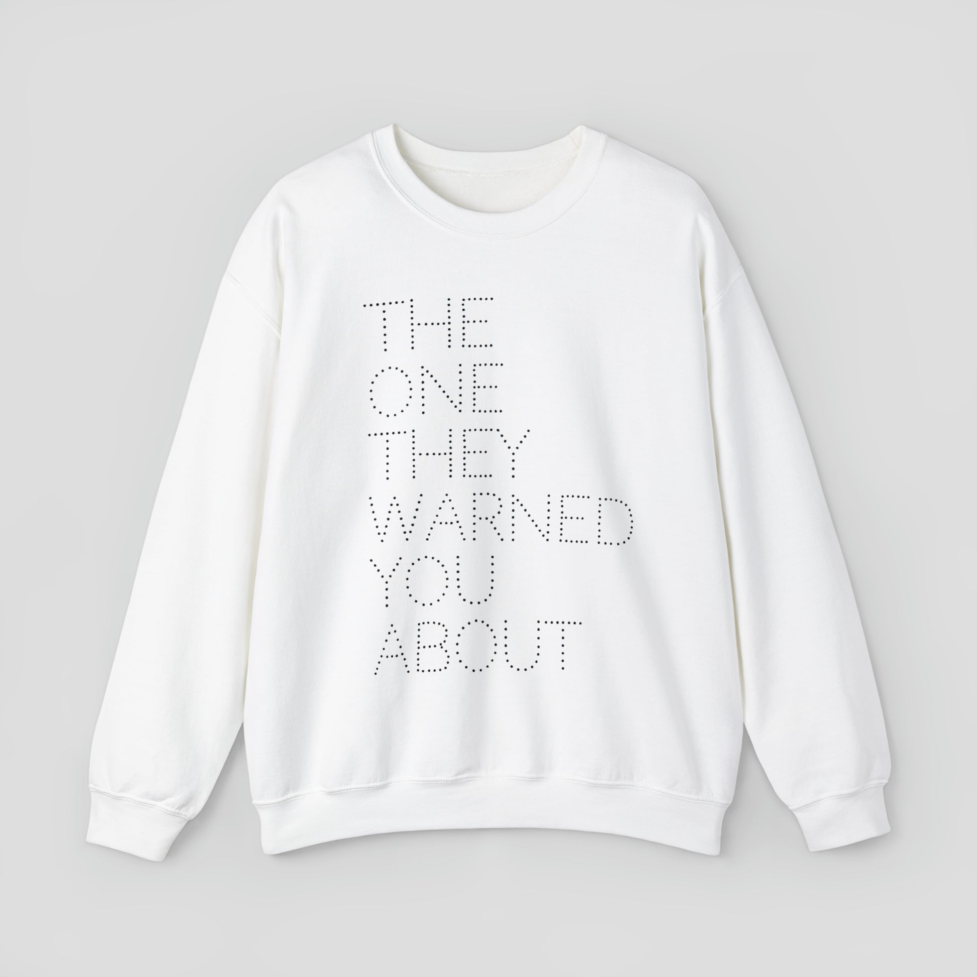 Front view of white sweatshirt with with the words "The One They Warned You About" in capitalized dotted text in center, against a gray background.