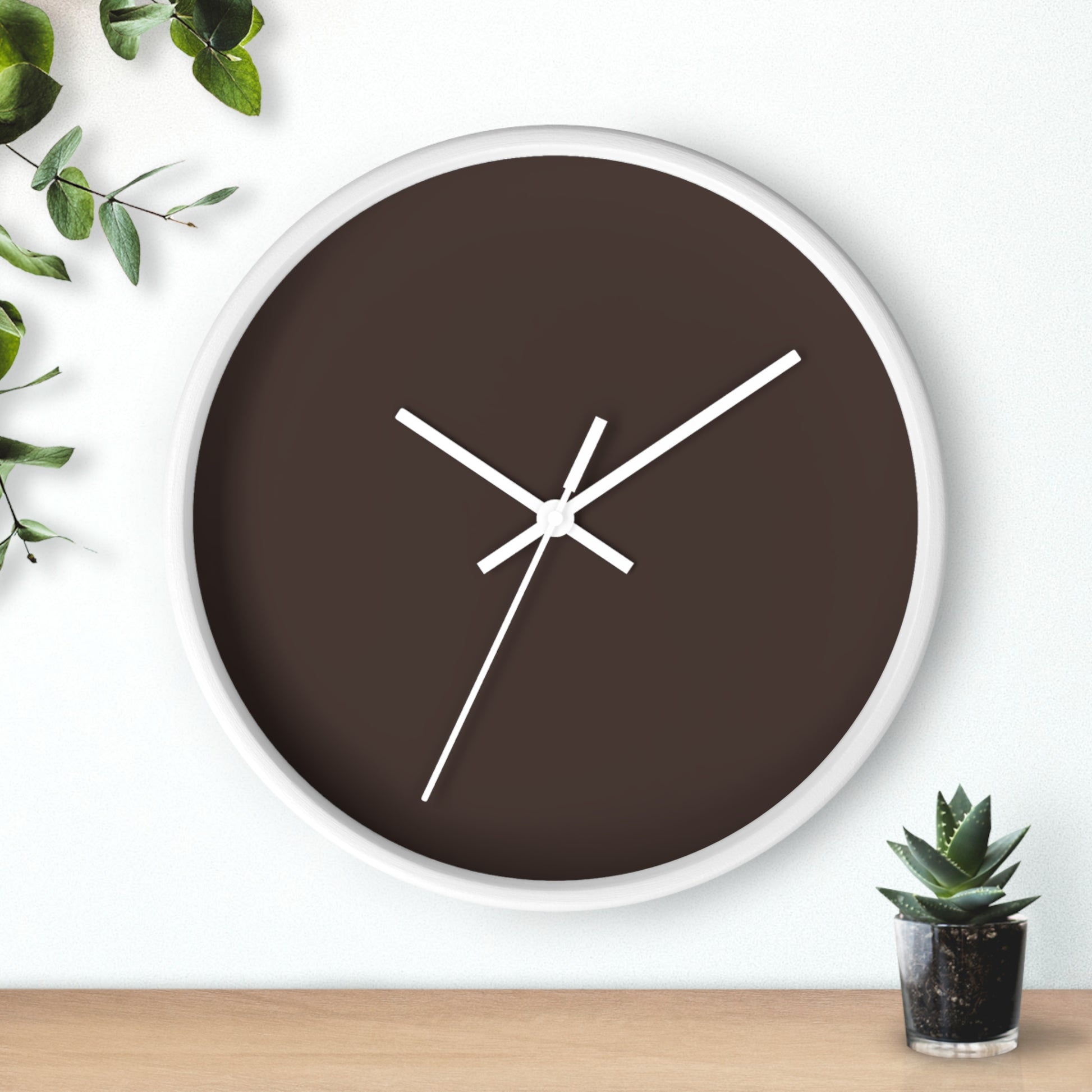 White circular wooden framed clock with espresso brown background and white hands with leaves on upper left corner and small cactus on bottom right.