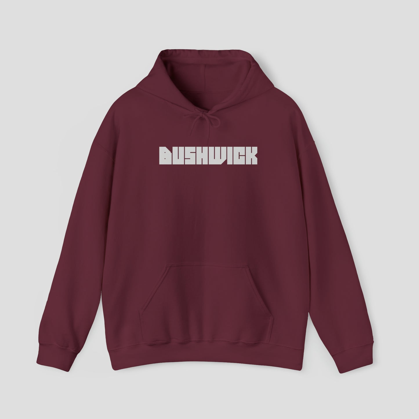 Front view of a maroon hooded sweatshirt with hood down and the word "Bushwick" in a large white block letters in center, against a gray background.