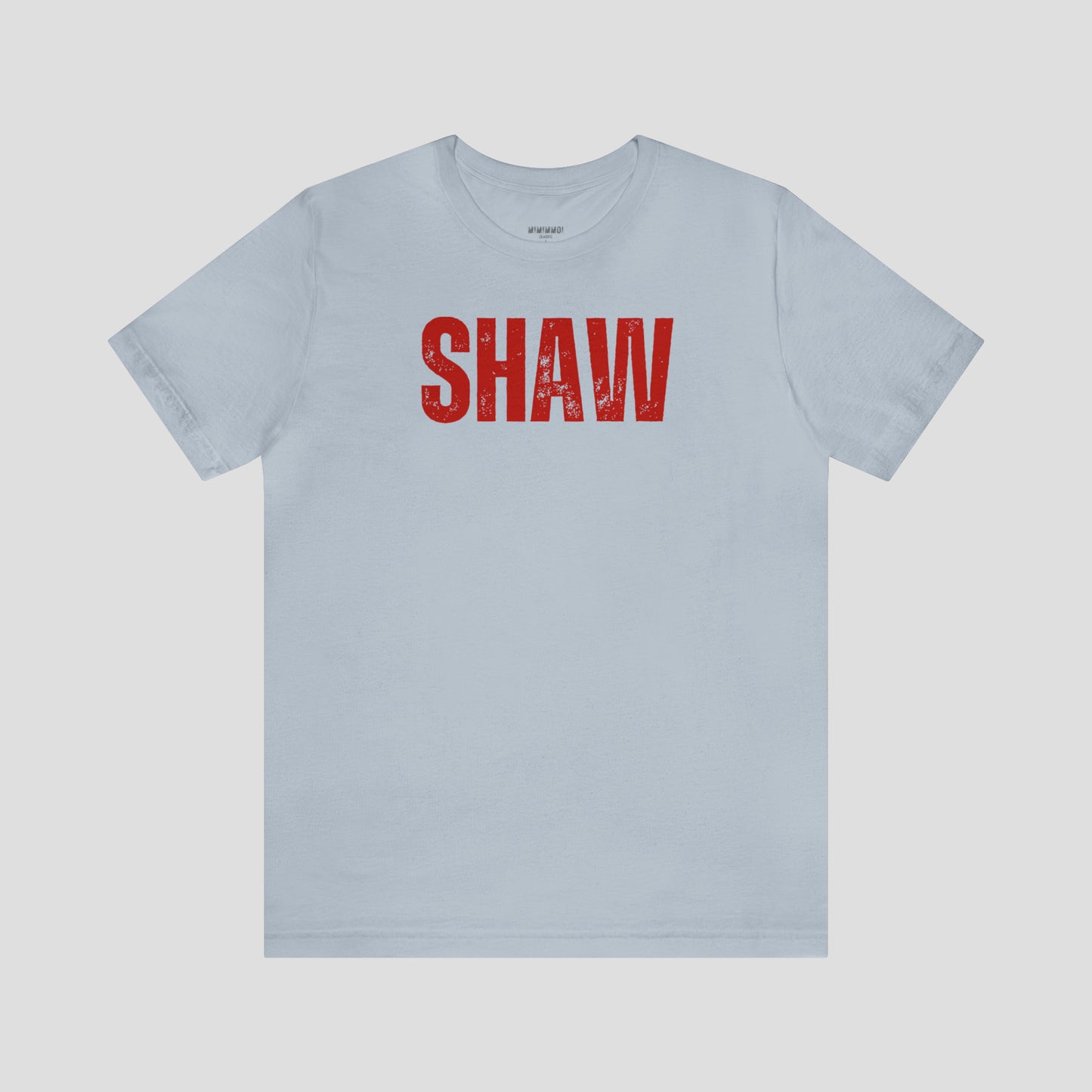 Light blue t-shirt with the word "Shaw" in large red, grunge block letters across the chest, against a gray background.